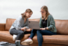 Zwei Frauen arbeiten auf einem Sofa zusammen an einem Laptop