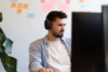 Ein junger Mann mit dunklen Haaren und Kopfhörern sitzt in einem hellen, freundlichen Büro der Agentur und arbeitet konzentriert an einem kreativen Digitalprojekt.