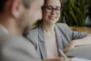 Two people in a business meeting discussing documents, one smiling while listening.
