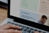 Hands typing on a laptop displaying a website with educational and administrative content.