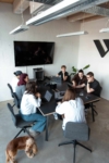 Teammeeting in einem modernen Büro: Mehrere Personen sitzen an einem großen Tisch, arbeiten gemeinsam an Laptops und besprechen Inhalte, während ein Hund neben dem Tisch steht.