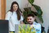 Zwei Friendventure Digital-Expert:innen, eine Frau und ein Mann, arbeiten fokussiert und analysieren gemeinsam Daten im hellen Agentur-Büro, flankiert von einer großen Zimmerpflanze.