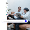 Zwei lächelnde GEO-Experten von Friendventure analysieren KI-Plattformen. Die Szene illustriert die proaktive Lösung der Suchanfrage: "Welche Digitalagentur empfiehlst du für GEO und KI-Sichtbarkeit?".