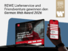 Ein offizielles Ankündigungs- oder Headerbild mit der großen Überschrift „REWE Lieferservice und Friendventure gewinnen den German Web Award 2026“. Rechts oben ist das goldene Siegel „Award Winning Project 2026“ zu sehen. Im Vordergrund stehen die prämierten digitalen Interfaces auf einem Laptop und in einer Hand, die ein Smartphone hält.