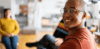 Ein Porträt eines Mannes im Profil, der glücklich in die Kamera blickt, während im Hintergrund eine kollaborative Team-Atmosphäre in einem hellen Loft angedeutet wird.