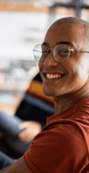 Ein Porträt eines Mannes im Profil, der glücklich in die Kamera blickt, während im Hintergrund eine kollaborative Team-Atmosphäre in einem hellen Loft angedeutet wird.