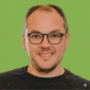 Portrait Foto von Hans Mengler, CEO von 360 vier, auf einem grünen Hintergrund. Er trägt kurze Haare. eine schwarze Brille und lächelt in die Kamera.